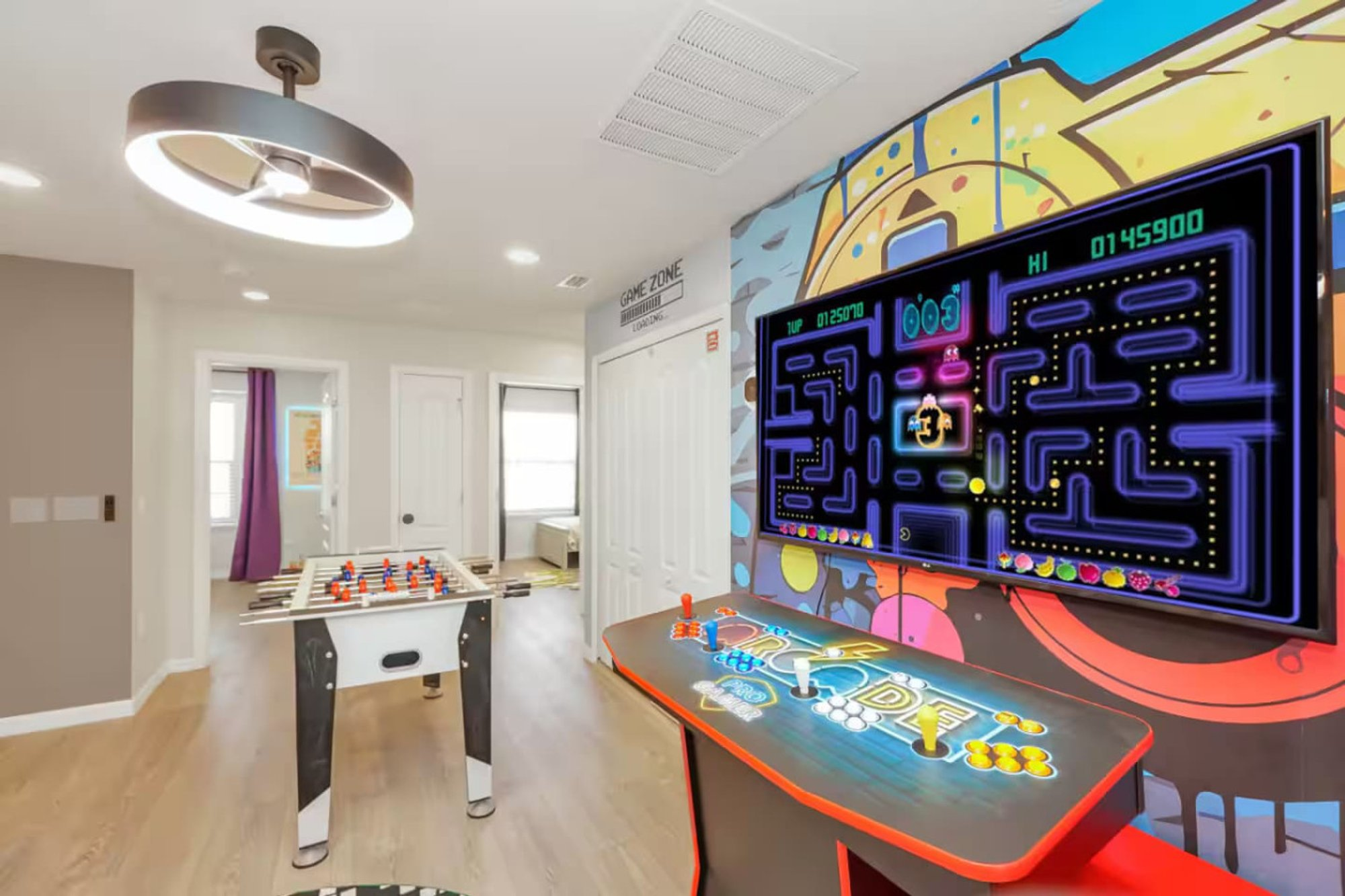 Arcade cabinet running Pac-Man in the game loft, with the foosball table behind