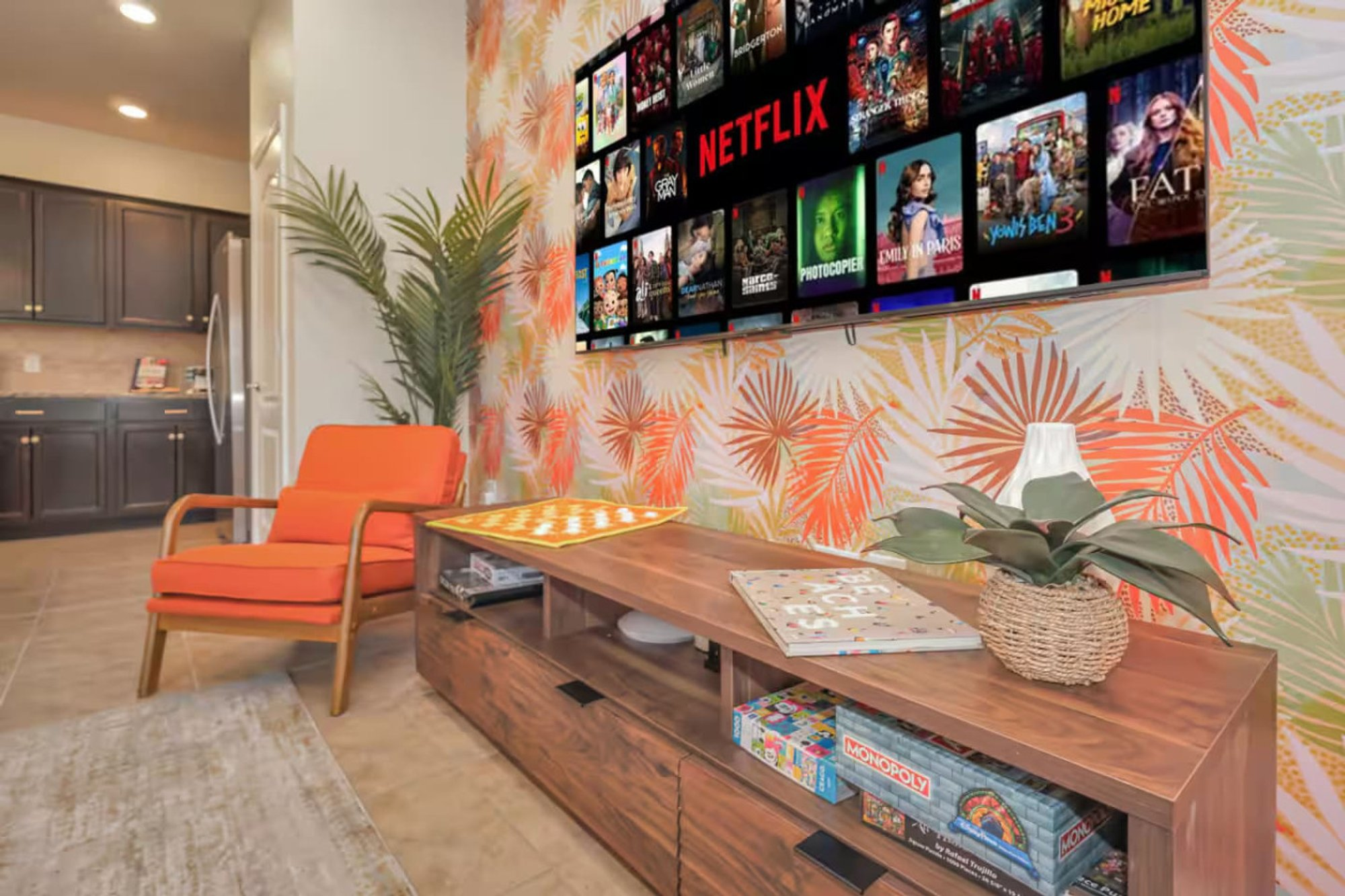 Media wall and orange armchair under the palm-print wallpaper